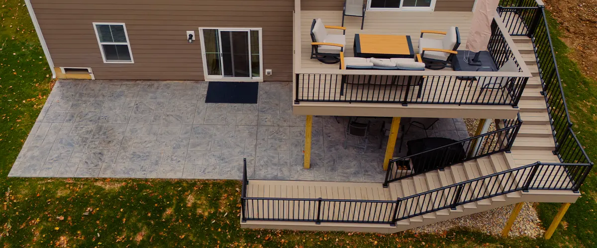 Modern two-level deck with black railings and outdoor seating, featuring a stamped concrete patio below.