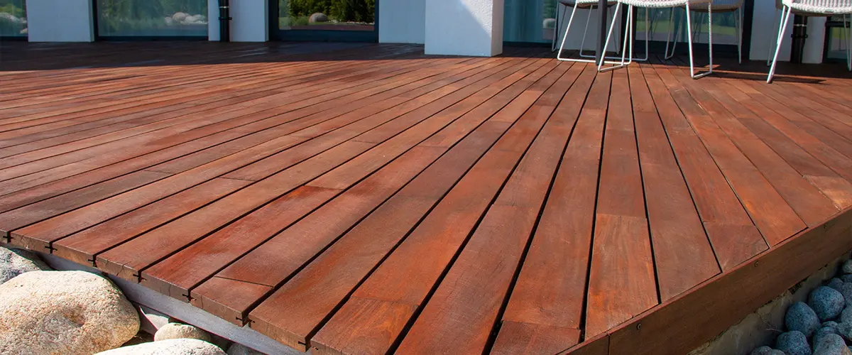 Modern dark wood deck with clean lines and white patio chairs outside a contemporary home with stone landscaping