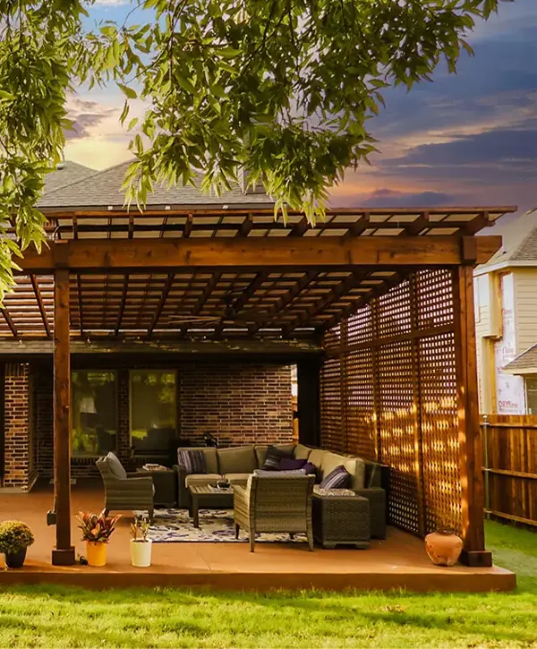A stunning, dark wood custom pergola installation covering an outdoor lounge and dining patio in Lawrence, IN. The structure includes a lattice roof for filtered shade and matching privacy lattice screens on the side.