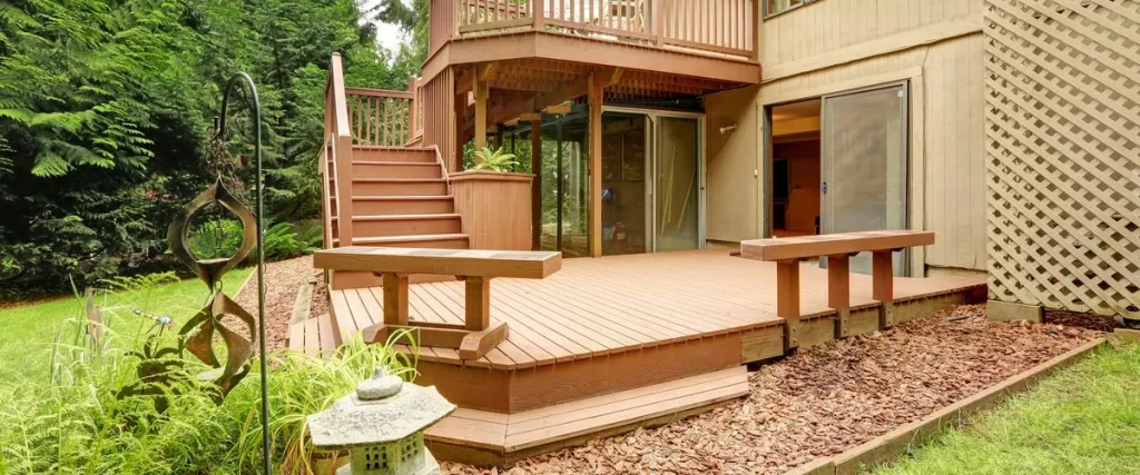 A stained wooden two-tiered deck featuring built-in benches, a set of access stairs, and a decorative garden area leading down to a lower level.