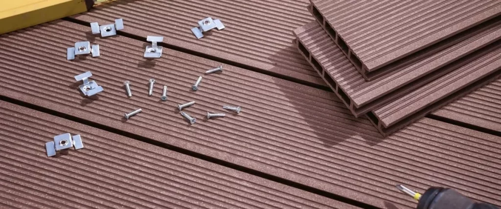 A detailed close-up view of brown wood-textured composite decking boards laid out with metal hidden fastening clips and silver screws for a DIY installation project.