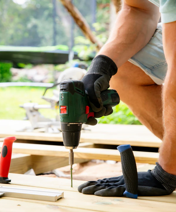 Professional contractor performing deck repair in Whitestown, IN by driving a screw into new wooden boards with a power drill.