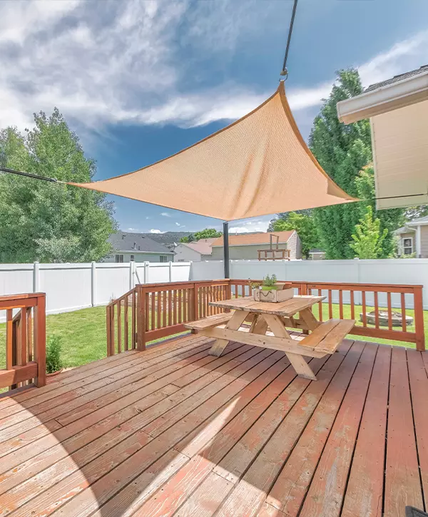 A sun-drenched wood deck in Lapel, IN featuring a triangular beige sun shade sail and a classic wooden picnic table.