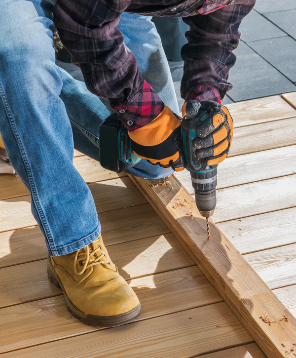 A close-up of a contractor performing deck repair in Lapel, IN, using a cordless power drill to create pilot holes in new light-colored wood boards.