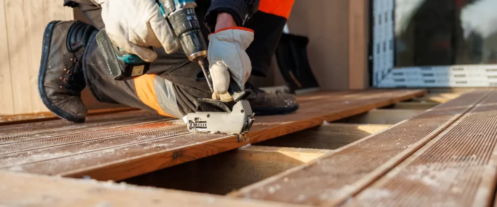 a deck builder installing timber or composite decking boards onto a wooden frame using a cordless drill and hidden fastening clips