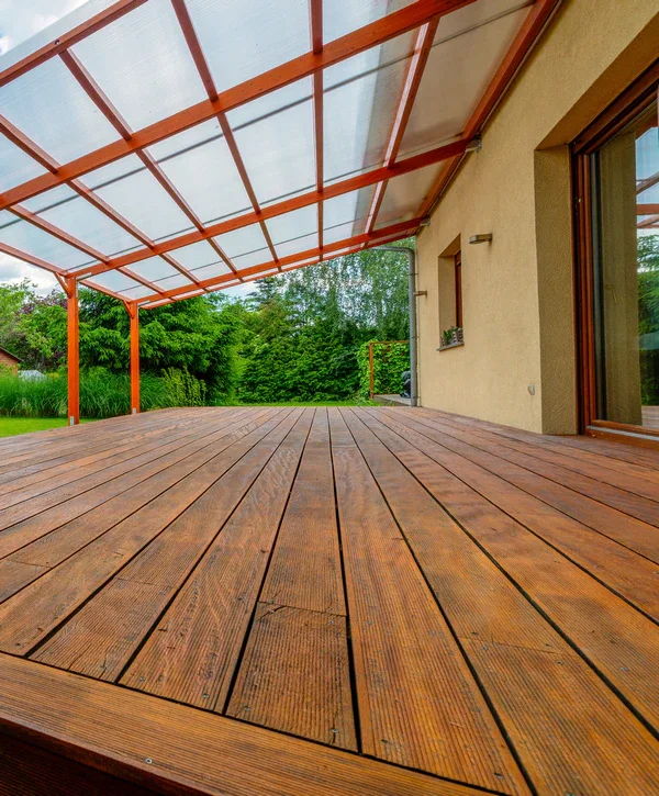 A freshly finished wooden deck featuring a translucent patio roof extension with orange-brown framing, overlooking a green backyard after a deck building project in Sheridan, IN.